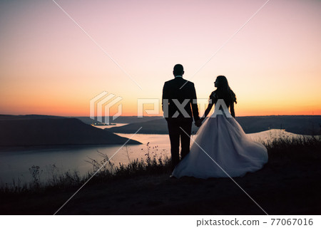 Silhouettes of bride and groom at night against lake and islands 77067016
