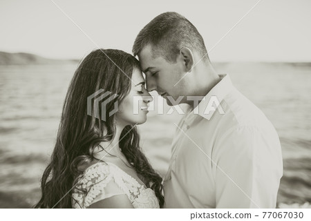 groom and bride stand in embrace on rocky bank near river in summer 77067030