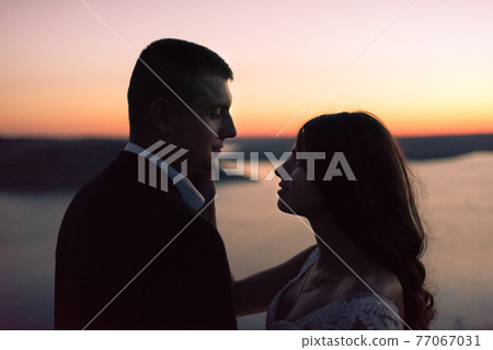 Silhouettes of bride and groom at night against lake and islands 77067031