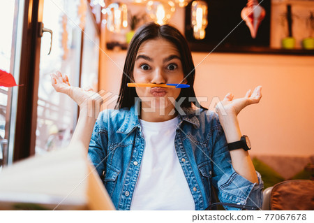 Young playful woman student holding pen between her nose 77067678