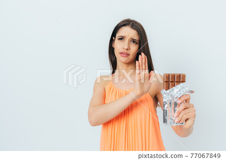 Beautiful young woman with stop gesture refuses eating chocolate bar 77067849