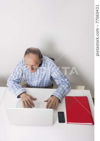 High angle view of senior businessman using laptop at office desk High angle view of senior businessman using laptop at office desk 77068431