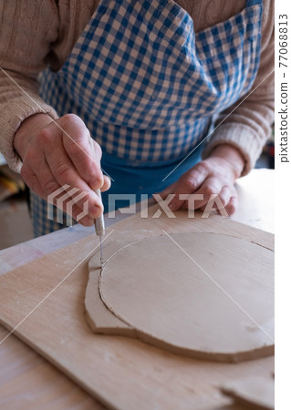 Senior female artist cutting wet clay creating a plate 77068813