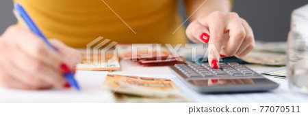 Woman is counting on calculator and writing with pen in notebook closeup 77070511