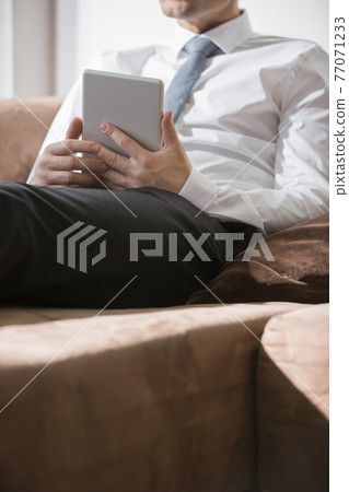 Midsection of businessman holding digital tablet on sofa at home 77071233