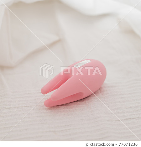 Close-up of a clitoral vibrator on a white sheet on the bed 77071236
