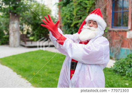 Santa claus in a protective costume puts on gloves. Santa claus in a protective costume puts on gloves. 77071303