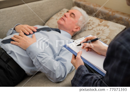An elderly man lies on a couch during an appointment with a psychotherapist. An elderly male patient in an individual consultation with a female psychologist An elderly man lies on a couch during an appointment with a psychotherapist. An elderly male patient in an individual consultation with a female psychologist 77071393