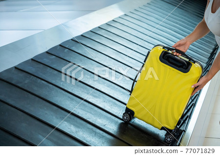 A woman takes a suitcase from the baggage carousel. A woman takes a suitcase from the baggage carousel. 77071829