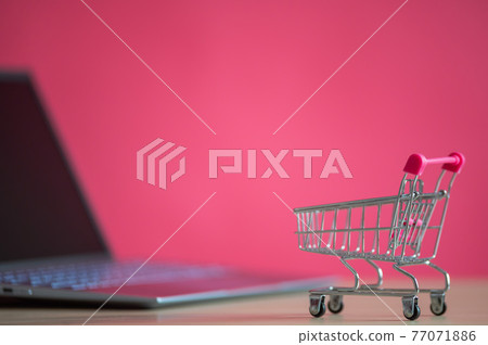 Online shopping concept. Mini grocery cart and laptop on a pink background. Small cart and personal computer. Online shopping concept. Mini grocery cart and laptop on a pink background. Small cart and personal computer. 77071886