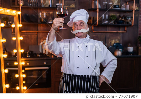 Portrait of friendly elderly male professional sommelier wearing apron and hat tasting red wine. Portrait of friendly elderly male professional sommelier wearing apron and hat tasting red wine. 77071907