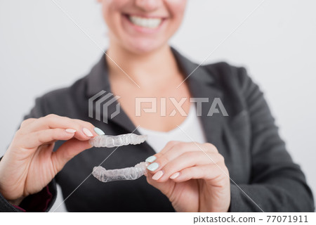A woman is holding a transparent plastic mouth guard. Orthodontist's bite correction device A woman is holding a transparent plastic mouth guard. Orthodontist's bite correction device 77071911