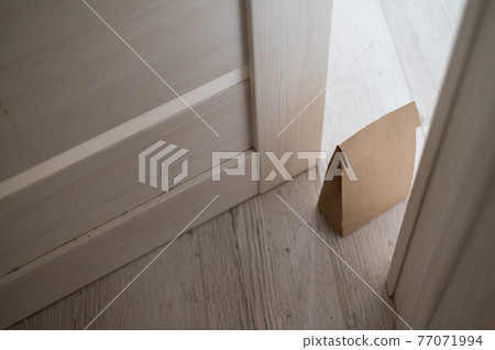 The concept of contactless delivery during the quarantine period. Kraft paper bag with online purchase at the open entrance door in case of danger of the spread of coronavirus. The concept of contactless delivery during the quarantine period. Kraft paper bag with online purchase at the open entrance door in case of danger of the spread of coronavirus. 77071994