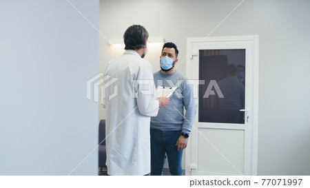 Male doctor speaking with patient in hospital hallway Male doctor speaking with patient in hospital hallway 77071997