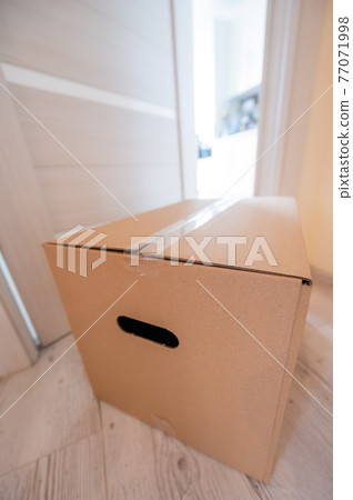 The concept of contactless delivery during the quarantine period. Cardboard box with online purchase at the open entrance door in case of danger of the spread of coronavirus. The concept of contactless delivery during the quarantine period. Cardboard box with online purchase at the open entrance door in case of danger of the spread of coronavirus. 77071998