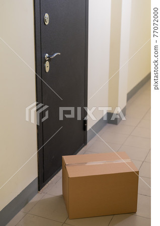 Contactless door delivery concept. Cardboard box with online purchase at the front door in the empty hall of an apartment building. Contactless door delivery concept. Cardboard box with online purchase at the front door in the empty hall of an apartment building. 77072000