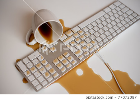 Spilled black coffee on a computer keyboard at a white table Spilled black coffee on a computer keyboard at a white table 77072087
