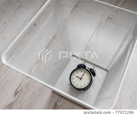 Top view of an alarm clock discarded in a white mesh metal trash bin. The concept of wasted time. 77072206