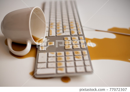 Spilled black coffee on a computer keyboard at a white table 77072307
