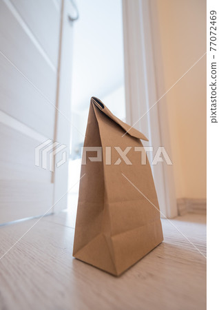 The concept of contactless delivery during the quarantine period. Kraft paper bag with online purchase at the open entrance door in case of danger of the spread of coronavirus. The concept of contactless delivery during the quarantine period. Kraft paper bag with online purchase at the open entrance door in case of danger of the spread of coronavirus. 77072469