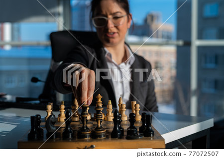 Business woman in a suit plays chess. Close-up of a female hand on a pawn 77072507