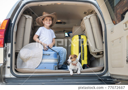 Happy boy in a cowboy hat and puppy jack russell terrier travel by car. A child and a funny little dog are sitting in the trunk and are ready for summer vacation. Independent travel. Best friends. Happy boy in a cowboy hat and puppy jack russell terrier travel by car. A child and a funny little dog are sitting in the trunk and are ready for summer vacation. Independent travel. Best friends. 77072687
