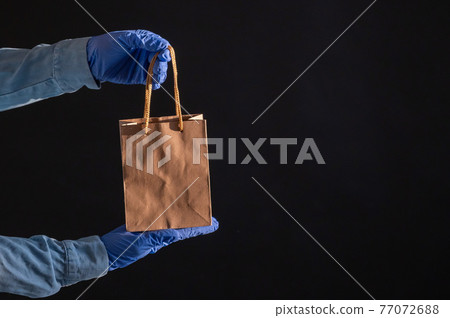 Express delivery to the epidemic of coronavirus. Closeup of courier's hands in rubber gloves with a paper bag with handles. Packaging made from eco friendly recycled material. Donation to quarantine. Express delivery to the epidemic of coronavirus. Closeup of courier's hands in rubber gloves with a paper bag with handles. Packaging made from eco friendly recycled material. Donation to quarantine. 77072688