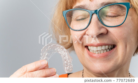 A happy elderly woman puts on transparent removable braces. Cosmetic dentistry for all ages A happy elderly woman puts on transparent removable braces. Cosmetic dentistry for all ages 77072689