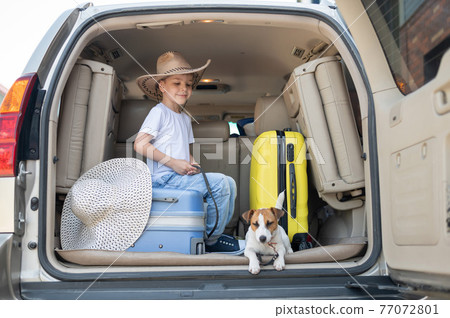 Happy boy in a cowboy hat and puppy jack russell terrier travel by car. A child and a funny little dog are sitting in the trunk and are ready for summer vacation. Independent travel. Best friends. Happy boy in a cowboy hat and puppy jack russell terrier travel by car. A child and a funny little dog are sitting in the trunk and are ready for summer vacation. Independent travel. Best friends. 77072801