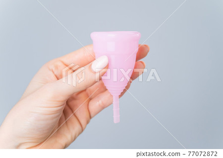 Close-up of a female hand with a pink menstrual cup on a white background. Caring for the environment. Eco friendly female intimate hygiene product. Close-up of a female hand with a pink menstrual cup on a white background. Caring for the environment. Eco friendly female intimate hygiene product. 77072872