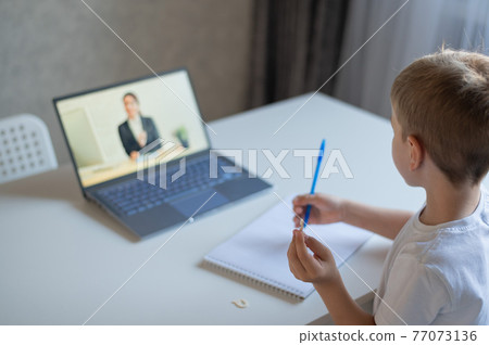 The boy communicates with a female teacher on a laptop webcam. Online lesson. Distance education in quarantine. A schoolboy is studying at home in the epidemic of coronavirus. 77073136