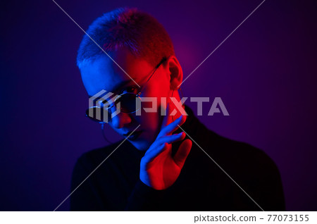 Portrait of a beautiful young woman with short hair in sunglasses in neon light 77073155