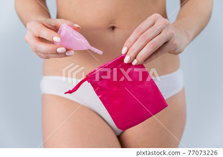A faceless Caucasian woman in underpants puts a pink menstrual cup in a small silk bag. Eco Friendly Products: Feminine intimate hygiene during menstruation A faceless Caucasian woman in underpants puts a pink menstrual cup in a small silk bag. Eco Friendly Products: Feminine intimate hygiene during menstruation 77073226
