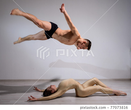 Acrobatic couple perform number on a white background. A duet of gymnasts rehearsing a performance with support. A man and a very flexible woman are dancing. Acrobatic couple perform number on a white background. A duet of gymnasts rehearsing a performance with support. A man and a very flexible woman are dancing. 77073816