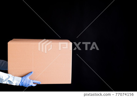 Closeup of female hands in gloves and a denim shirt. Delivery man holds a cardboard box to the customer on a black background. Antimicrobial protection in an epidemic. Closeup of female hands in gloves and a denim shirt. Delivery man holds a cardboard box to the customer on a black background. Antimicrobial protection in an epidemic. 77074156