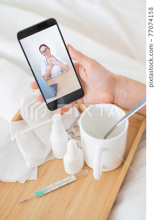 Close-up of female hands holding a phone with a doctor on the screen. Remote appointment with a doctor. A woman on sick leave is talking to the attending physician. Close-up of female hands holding a phone with a doctor on the screen. Remote appointment with a doctor. A woman on sick leave is talking to the attending physician. 77074158
