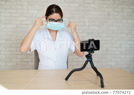 Remote appointment with a physician in quarantine. A doctor shows how to wear a medical mask for protection at an online telephone consultation. 77074272