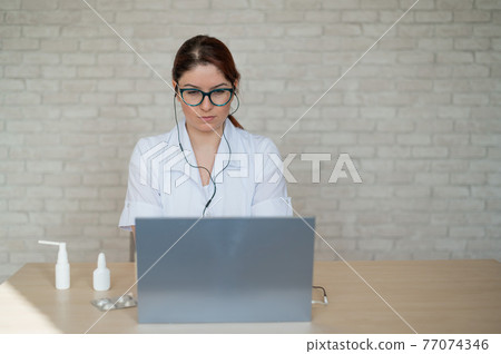 A female doctor conducts an online consultation. Remote reception at the therapist in quarantine. Medic woman recommends medication to the patient live. Insulation. 77074346