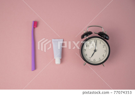 Toothbrush, tube of toothpaste and alarm clock on a pink background. Time to brush your teeth. Toothbrush, tube of toothpaste and alarm clock on a pink background. Time to brush your teeth. 77074353