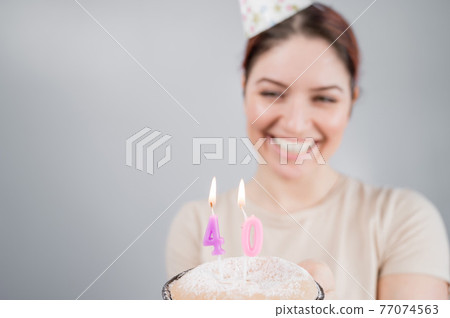 The happy woman makes a wish and blows out the candles on the 40th birthday cake. Girl celebrating birthday. Copy space. The happy woman makes a wish and blows out the candles on the 40th birthday cake. Girl celebrating birthday. Copy space. 77074563
