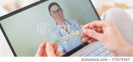 A woman is lying in bed with heat and is holding a thermometer. A friendly doctor talks to a sick patient by video link. Therapist on a laptop screen. Online medical consultation during the quarantine A woman is lying in bed with heat and is holding a thermometer. A friendly doctor talks to a sick patient by video link. Therapist on a laptop screen. Online medical consultation during the quarantine 77074567