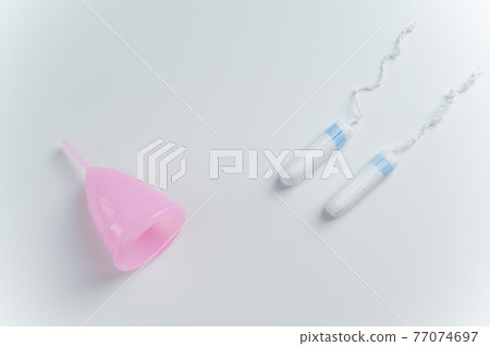 Pink menstrual cup and tampons on a white background. Comparison of personal hygiene products for women during menstruation Pink menstrual cup and tampons on a white background. Comparison of personal hygiene products for women during menstruation 77074697