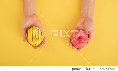 Female hands with donuts on a yellow background. Copy space. Female hands with donuts on a yellow background. Copy space. 77074788