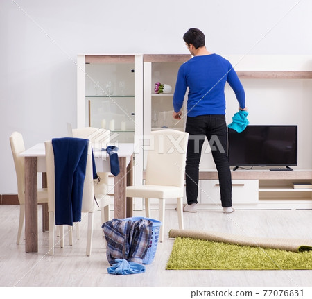 Young man collecting dirty clothing for laundry 77076831