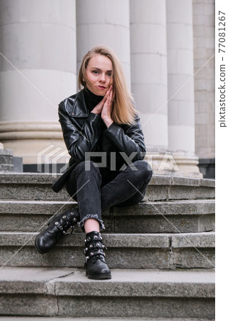 Portrait of young blonde woman with red lips wearing leather jacket on corporate building stairs. Career businesswoman. Urban street city lifestyle 77081267