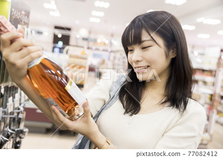 一位女顧客很高興在超市找到她正在尋找的葡萄酒 一位女顧客很高興在超市找到她正在尋找的葡萄酒 77082412