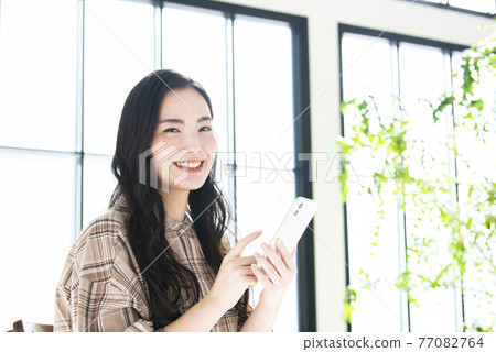 A young woman searching on a smartphone looking at the camera A young woman searching on a smartphone looking at the camera 77082764