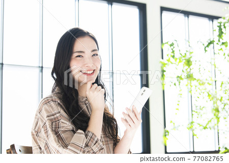 A young woman searching on a smartphone looking at the camera A young woman searching on a smartphone looking at the camera 77082765