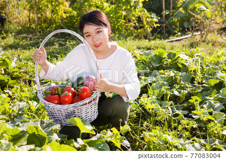 Sitting woman holding basket of vegetables Sitting woman holding basket of vegetables 77083004