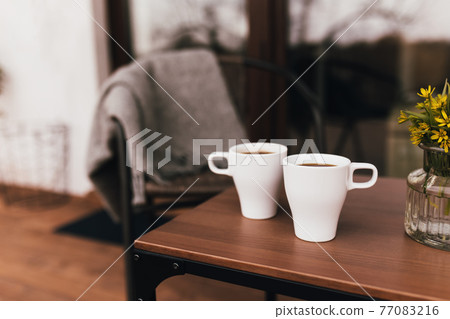 Two cups of coffee on the table on wooden brown terrace during evening sunset 77083216
